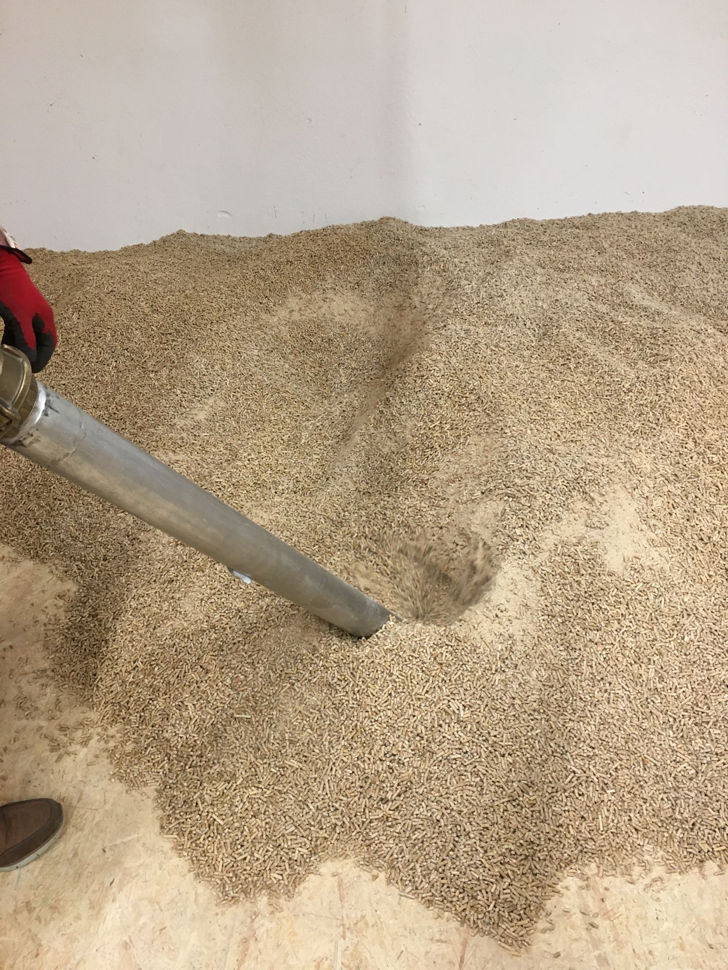 Das Bild zeigt ein nahezu leeres Pelletlager aus Spanplatten. Der letzte Rest Pellets wird gerade noch von einem Mitarbeiter der Schellinger KG abgesaugt. 