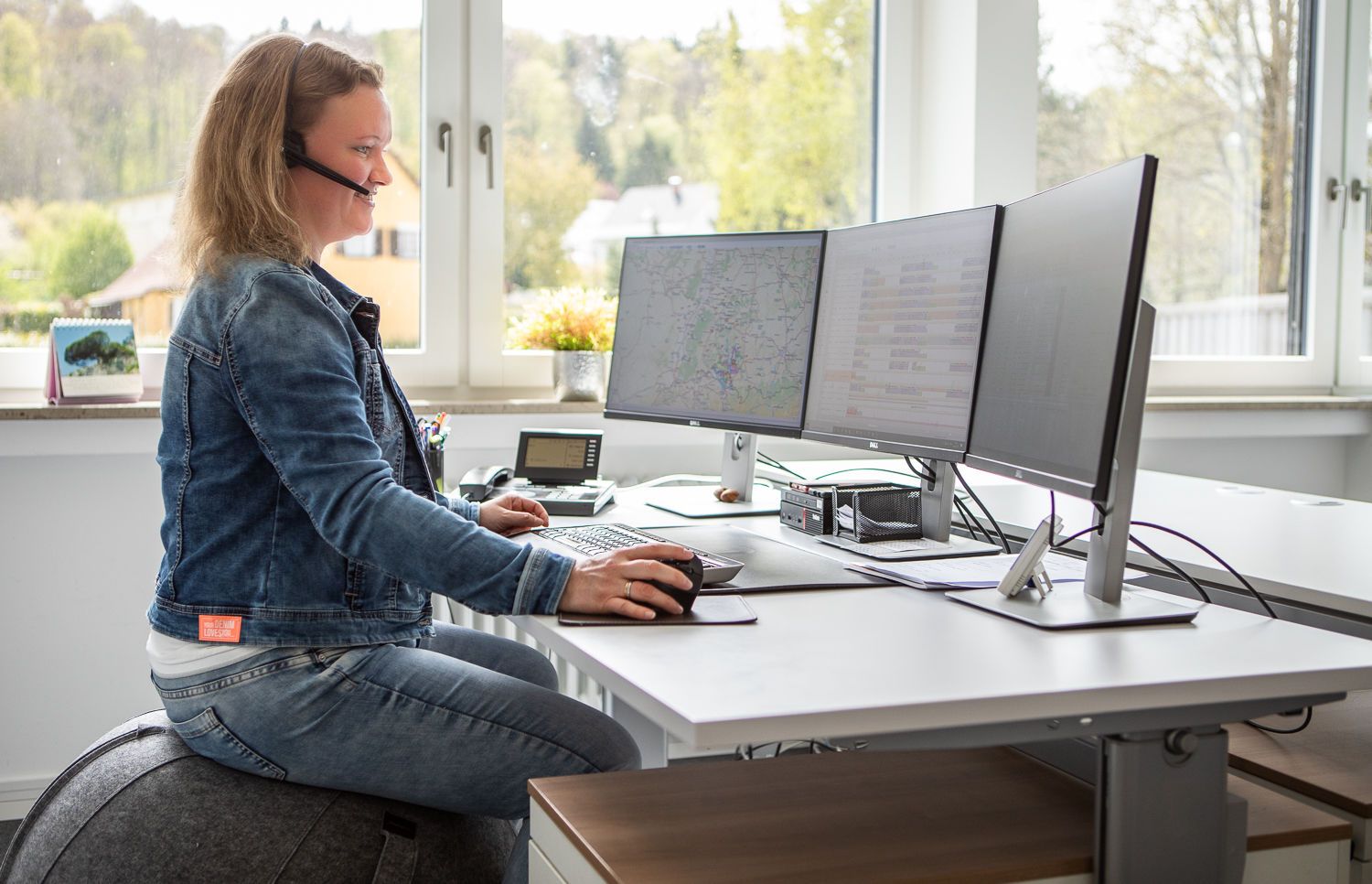 Mitarbeiterin Ramona Kresser sitzt am Schreibtisch auf einem Gymnastikball und arbeitet am PC in der Logistik Abteilung.